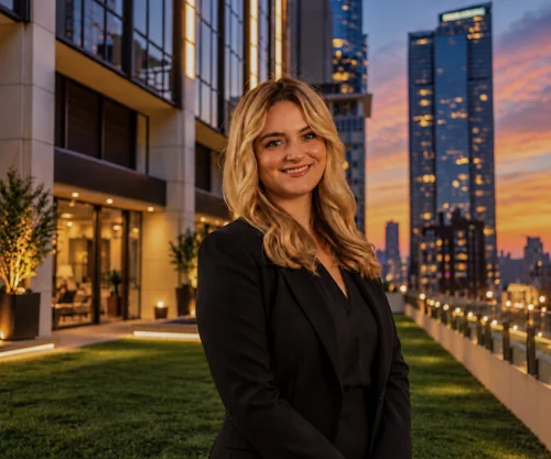 Woman in a black blazer photographed outdoors with city buildings at dusk