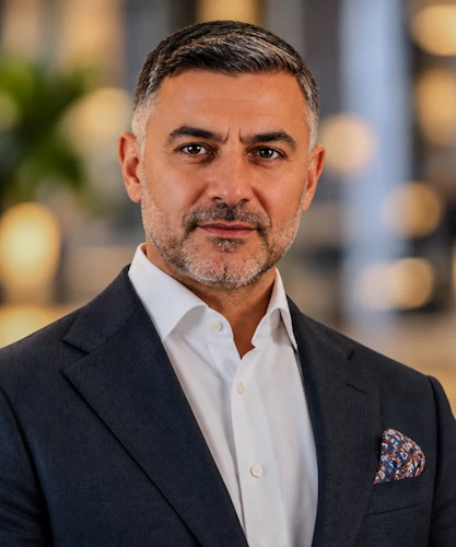 Professional headshot of a man in a navy blazer and white shirt against a softly blurred background, by ConstructaVision 360
